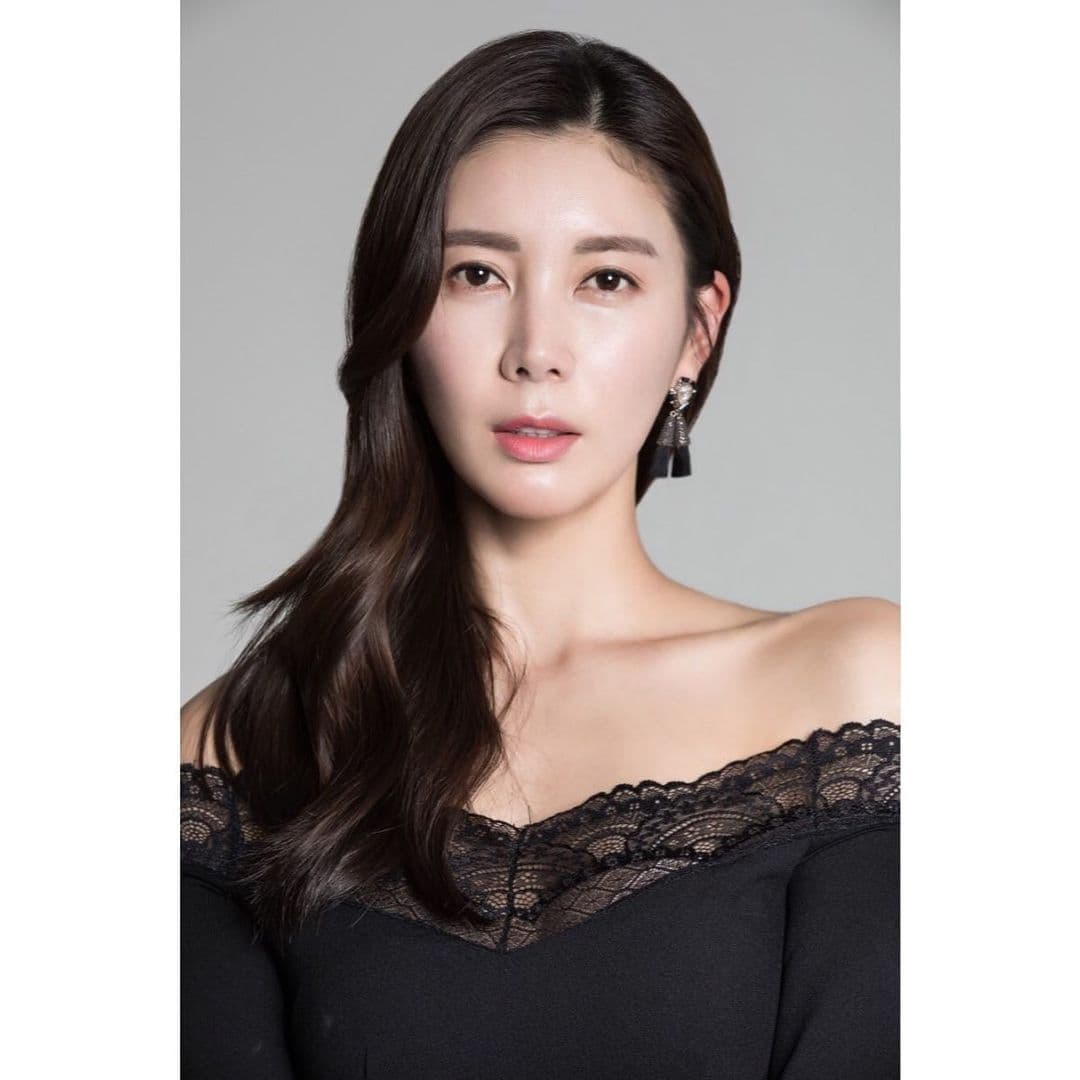 Woman with long dark hair wearing a black off-the-shoulder top with lace trim.